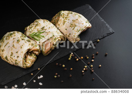 Chicken half-cooked thighs. Top of view. Raw chicken marinated.Copy space.Raw marinated chicken thighs in a light sauce with herbs and spices on a dark background with herbs. 88634008
