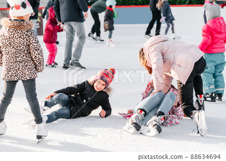 Soft,Selective focus.People, friendship, sport and leisure concept - happy friends on skating rink.Group of teenage friends ice skating on an ice rink.A kid takes relax after his fall while skating. 88634694