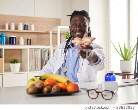 Afroamerican nutritionist looking at camera and showing healthy fruits in the consultation. Afroamerican nutritionist looking at camera and showing healthy fruits in the consultation. 88638058