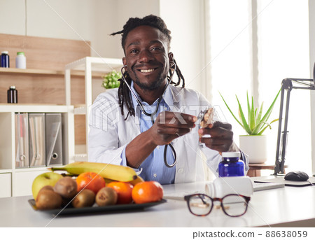 Afroamerican nutritionist looking at camera and showing healthy fruits in the consultation. Afroamerican nutritionist looking at camera and showing healthy fruits in the consultation. 88638059