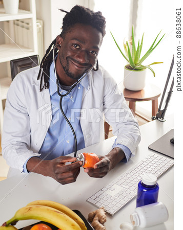 Afroamerican nutritionist looking at camera and showing healthy fruits in the consultation. Afroamerican nutritionist looking at camera and showing healthy fruits in the consultation. 88638061