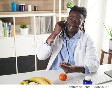 Afroamerican nutritionist looking at camera and showing healthy fruits in the consultation. Afroamerican nutritionist looking at camera and showing healthy fruits in the consultation. 88638062