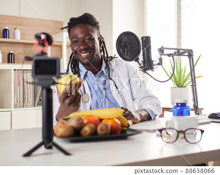 Afroamerican nutritionist looking at camera and showing healthy fruits in the consultation. Afroamerican nutritionist looking at camera and showing healthy fruits in the consultation. 88638066