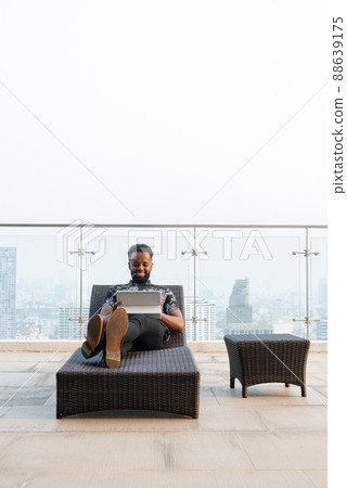 African man relaxing outdoors while using laptop computer and mobile phone 88639175