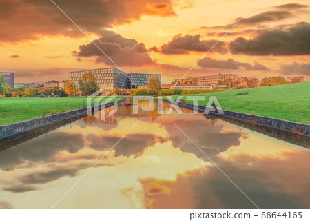 Beautiful yellow sunset with clouds over a river channel with reflection in a park overlooking residential buildings and a metro station DR Byen in the city area orestad. Copenhagen, Denmark 88644165