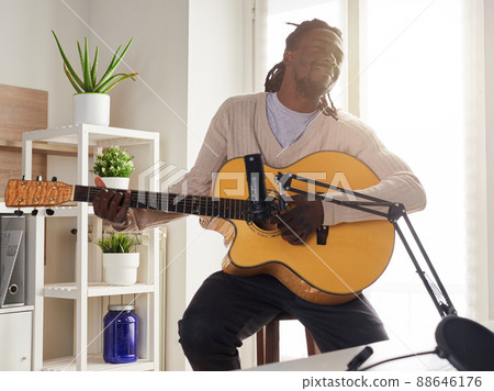 Young man is singing and playing guitar while making an audio recording at home 88646176