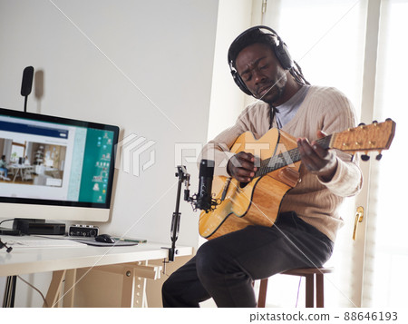 Young man is singing and playing guitar while making an audio recording at home Young man is singing and playing guitar while making an audio recording at home 88646193