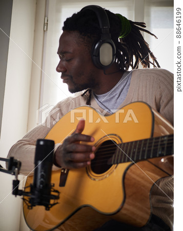 Young man is singing and playing guitar while making an audio recording at home Young man is singing and playing guitar while making an audio recording at home 88646199