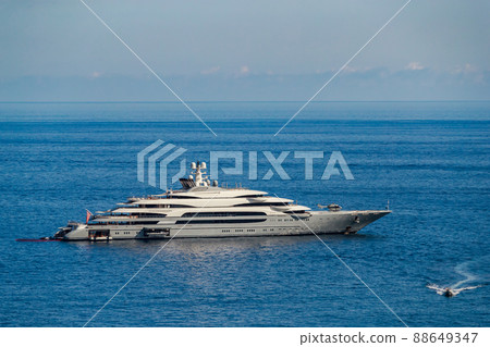 The huge mega yacht is moored in sea off the coast of the azur coastline at sunny day, the chrome plated handrail, sun reflection on glossy board of the motor boat 88649347
