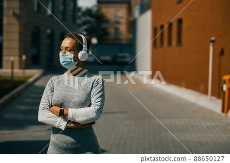Athletic woman in sportswear listening to music using headphones and looking aside during Covid 19 pandemic 88650127