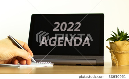 2022 agenda new year symbol. Tablet with words 2022 agenda. Businessman hand with pen, house plant. Copy space. Beautiful white background. Business, 2022 agenda new year concept, copy space. 88650961