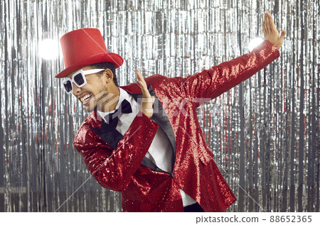 Funny young black guy in a sequin jacket, top hat and sunglasses dancing at a party Funny young black guy in a sequin jacket, top hat and sunglasses dancing at a party 88652365
