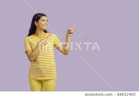 Young smiling woman pointing fingers at content copy space on pastel purple background. 88652405