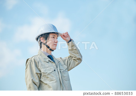 A young man in work clothes standing in a helmet against the blue sky A young man in work clothes standing in a helmet against the blue sky 88653033