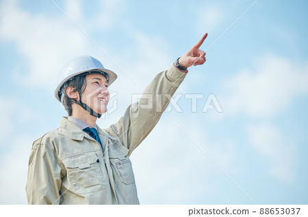 A young man in work clothes standing pointing against the blue sky A young man in work clothes standing pointing against the blue sky 88653037