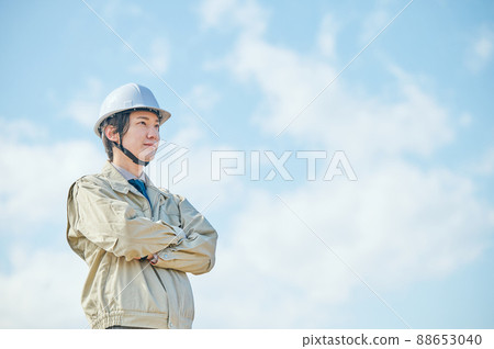 A young man in work clothes standing with his arms folded against the blue sky A young man in work clothes standing with his arms folded against the blue sky 88653040