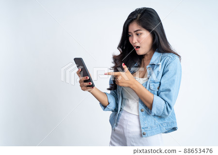 Young woman shocked with finger pointing using a mobile phone Young woman shocked with finger pointing using a mobile phone 88653476