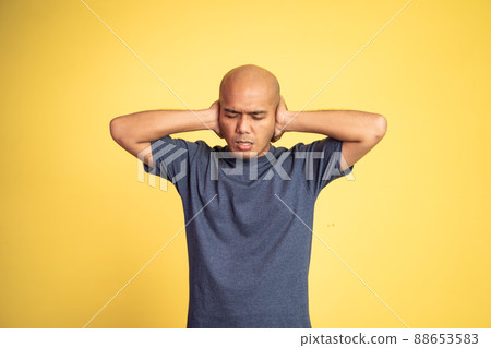 bald man with uncomfortable expression with hands covering ears 88653583