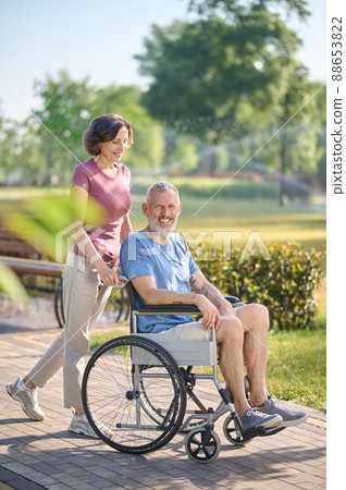 A dark-haired woman carrying her husband in a wheel chair 88653822