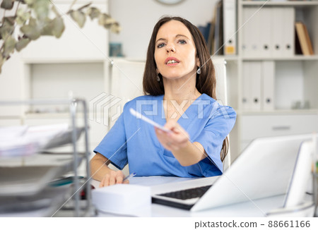 Woman physician giving recipe, sitting at table in office Woman physician giving recipe, sitting at table in office 88661166