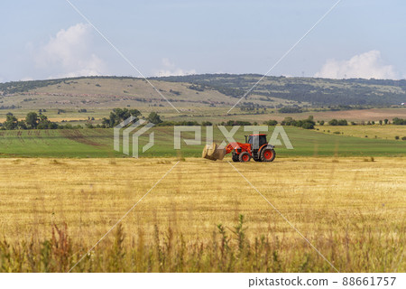 Tractor lifting hay bale on barrow. 88661757