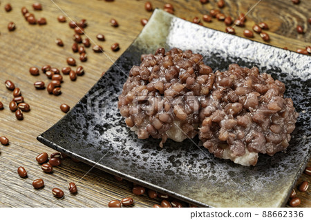 A dark wood-grained back with a black plate full of bean paste and azuki beans scattered randomly 88662336