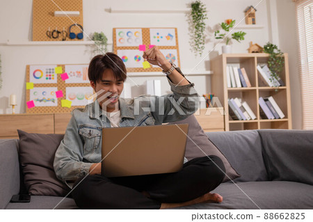 Enjoying the moment. At work, an Asian businessman sits at his desk with his laptop, tablet, and documents, looking well and pleased. 88662825