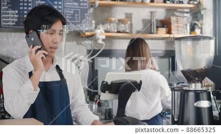 barista man coffee maker receive phone call and record pre order to computer in coffee cafe shop 88665325