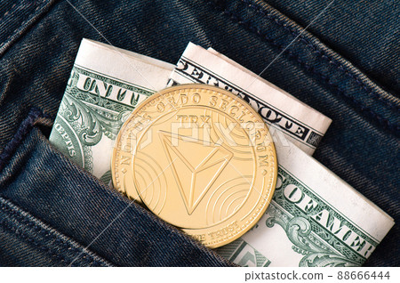 A golden physical TRON coin and folded dollars sticks out of the pocket of black jeans  88666444