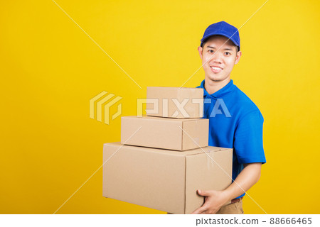 Portrait excited attractive delivery happy man logistic standing he smile wearing blue t-shirt and cap uniform holding parcel box looking to camera Portrait excited attractive delivery happy man logistic standing he smile wearing blue t-shirt and cap uniform holding parcel box looking to camera 88666465