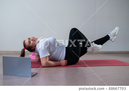 A chubby young woman is watching an online fitness lesson on a laptop. Distance sports training. A chubby young woman is watching an online fitness lesson on a laptop. Distance sports training. 88667703