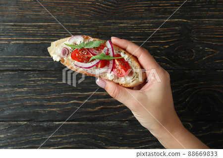 Female hand holds bruschetta on rustic wooden background Female hand holds bruschetta on rustic wooden background 88669833