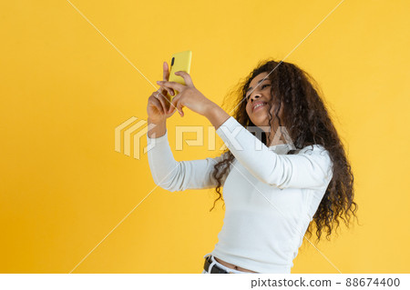 Young woman taking selfie on yellow background Young woman taking selfie on yellow background 88674400