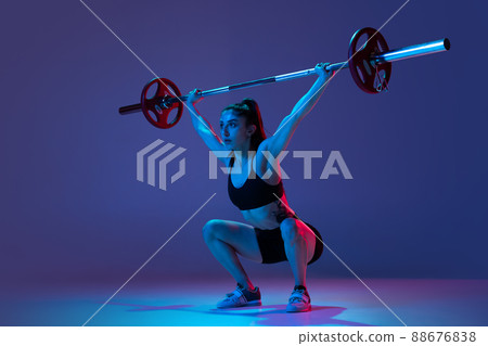 Portrait of muscled woman in sportswear training with a barbell isolated on purple background in neon light. Sport, weightlifting concept 88676838