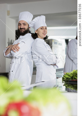Skilled cooks wearing cooking uniforms while posing back to back in restaurant kitchen space. Multiethnic gastronomy experts standing in arms crossed while smiling at camera. Skilled cooks wearing cooking uniforms while posing back to back in restaurant kitchen space. Multiethnic gastronomy experts standing in arms crossed while smiling at camera. 88677036