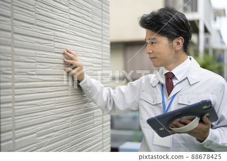 A middle-aged man in work clothes holding a tablet and investigating the outer wall A middle-aged man in work clothes holding a tablet and investigating the outer wall 88678425