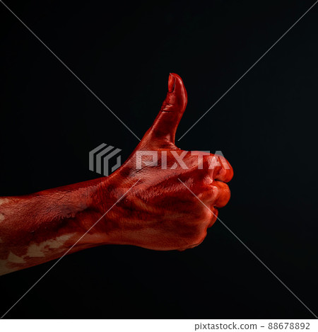 A woman's hand stained with blood shows a thumbs up on a black background.  88678892