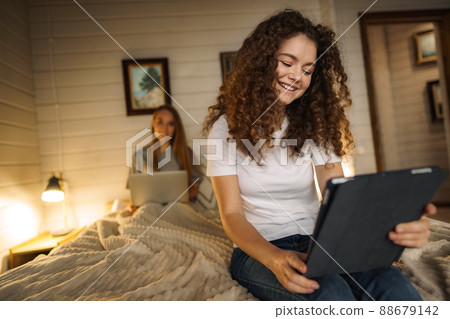 Two beautiful women lying in bed, holding a laptop 88679142