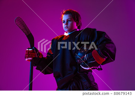 Half-length portrait of boy, child in protective uniform for hockey isolated over purple studio background in neon light. Concept of team sport 88679143