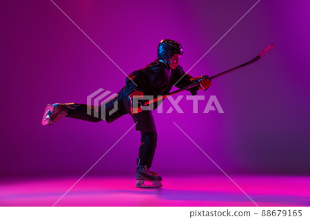 Portrait of boy, child, hockey player training, practising isolated over purple background in neon light. In action 88679165