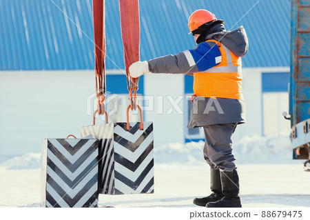 Professional slinger in construction helmet at factory unloads cargo. Boot training. Worker in warm 88679475