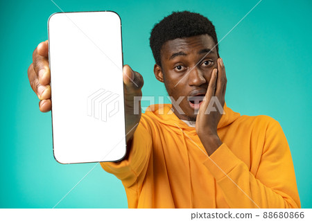 Smiling casual black man pointing at blank white cell phone screen in studio Smiling casual black man pointing at blank white cell phone screen in studio 88680866