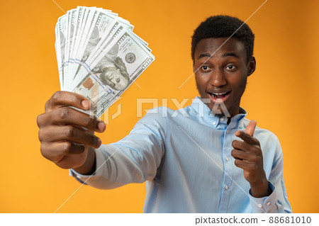 Excited black guy holding stack of Dollars in yellow studio 88681010