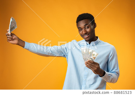 Excited black guy holding stack of Dollars in yellow studio Excited black guy holding stack of Dollars in yellow studio 88681523