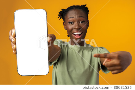 Young smiling african american woman showing smartphone with blank screen against yellow background Young smiling african american woman showing smartphone with blank screen against yellow background 88681525