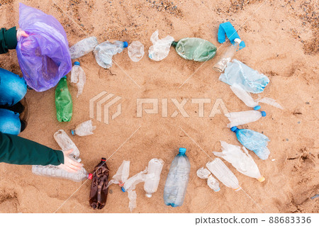 Ecology template. Volunteer picking up a garbage. Frame from plastic dirty bottles with copy space on a sandy beach. Top view. The concept of environmental protection and Earth Day 88683336