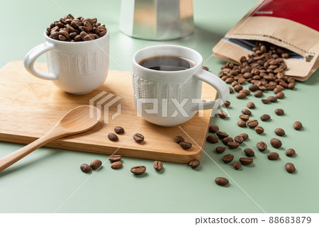 Cup of freshly brewed coffee, spoon and scattered coffee beans on a pastel green background. Cup of freshly brewed coffee, spoon and scattered coffee beans on a pastel green background. 88683879