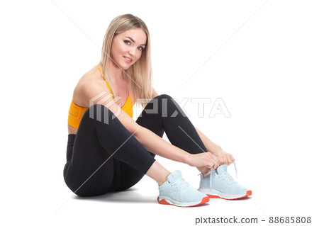 A beautiful, athletic, slim, smiling and cheerful woman in an orange top and black sweatpants is sitting and tying her shoelaces on sports sneakers. Lifestyle concept with sports and gym, healthy A beautiful, athletic, slim, smiling and cheerful woman in an orange top and black sweatpants is sitting and tying her shoelaces on sports sneakers. Lifestyle concept with sports and gym, healthy 88685808