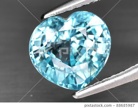 Natural gemstone blue zircon in tongs on a gray background 88685987