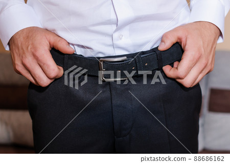 The groom tightens his belt. A man holding his hands on his belt 88686162